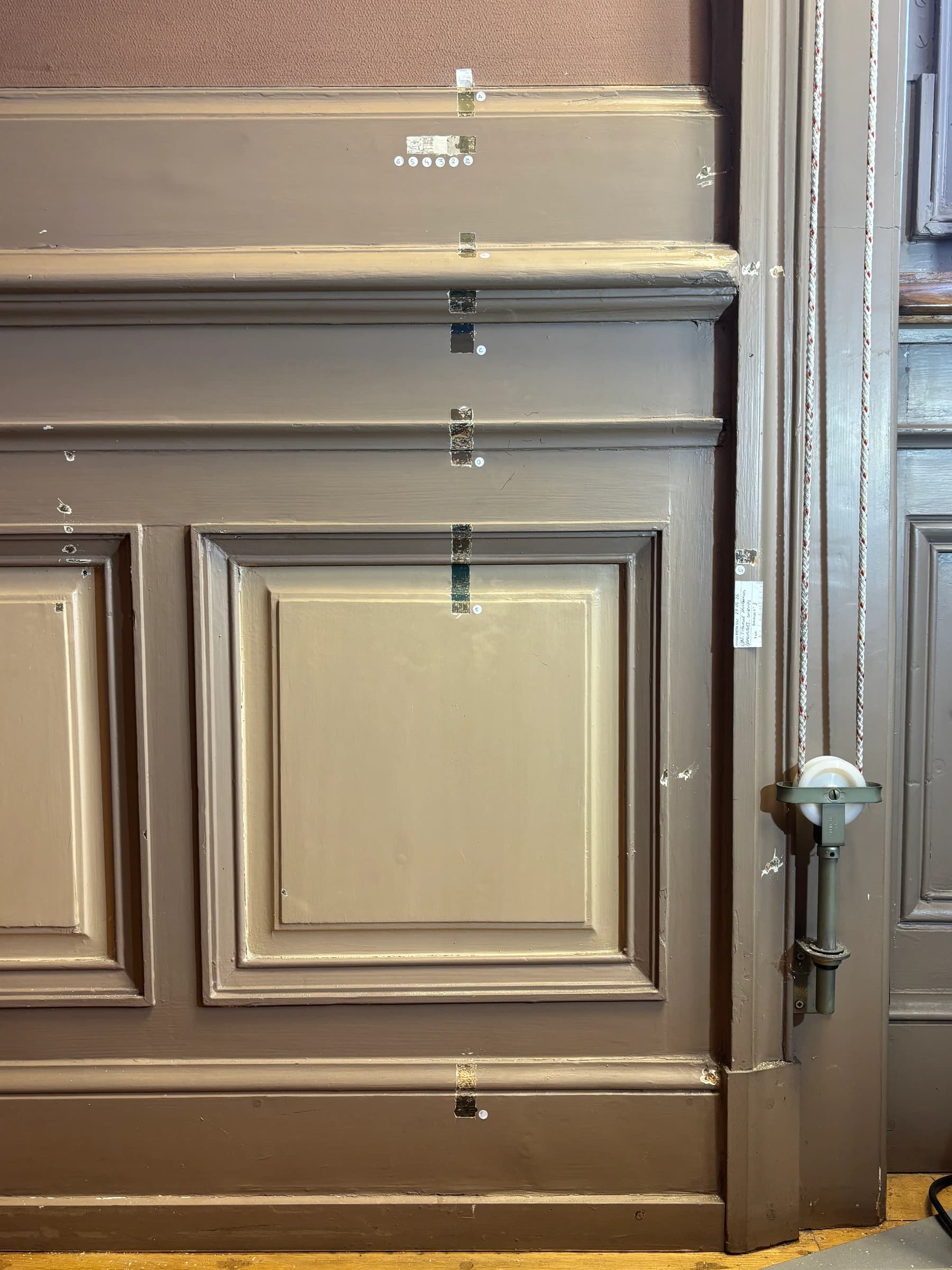 Painted wood panelling in its documented state, with numbered paint-layer investigation windows across the mouldings and panels.